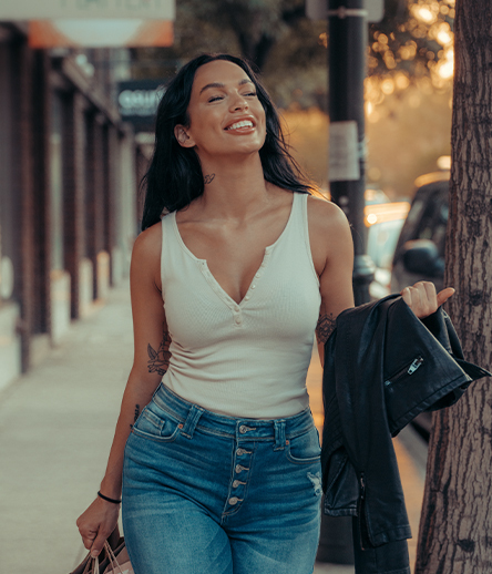 Smiling woman walking down the street holding a leather jacket